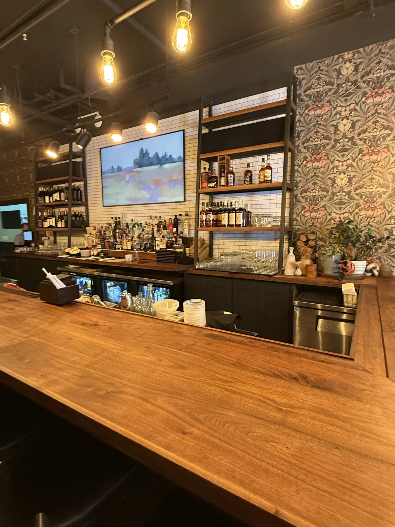 Restaurant bar with wood counter, warm lights, bottles, white tile and framed artwork
