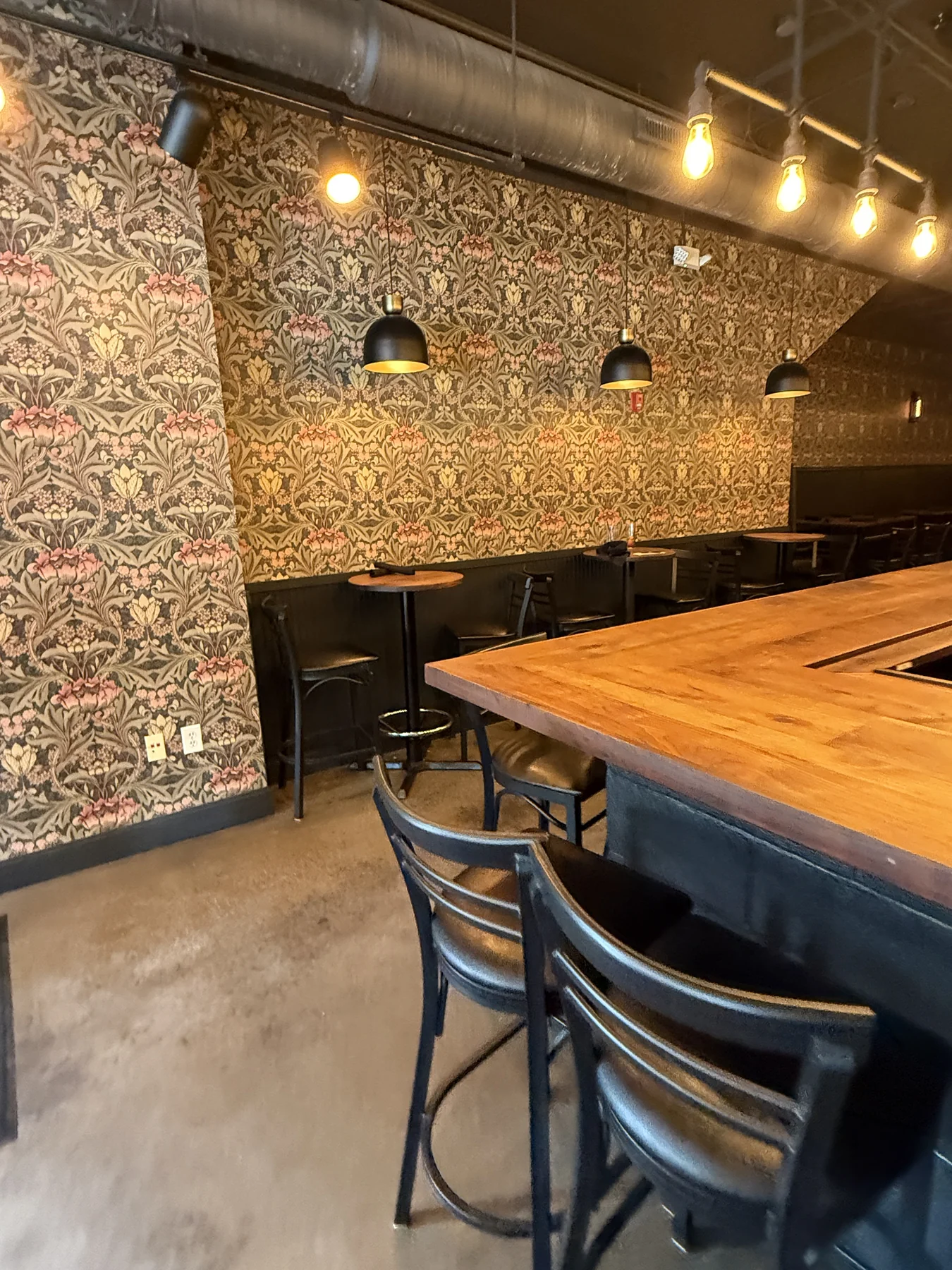 Warm dining room with wood tables, black seating, pendant lights and patterned wall covering